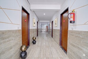 A hotel corridor with marble floors, wooden doors, numbered room signs, and a fire extinguisher. - Fabhotel Hr Residency (New Delhi)