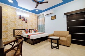 A bedroom with a bed, a sofa, a small table, a ceiling fan, and an air conditioning unit. - Fabhotel Luxe Cozy (Varanasi)