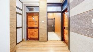 A narrow hallway with wooden flooring, a wooden door with a number plate, and a staircase leading to an upper level. - Fabhotel Luxe Cozy (Varanasi)