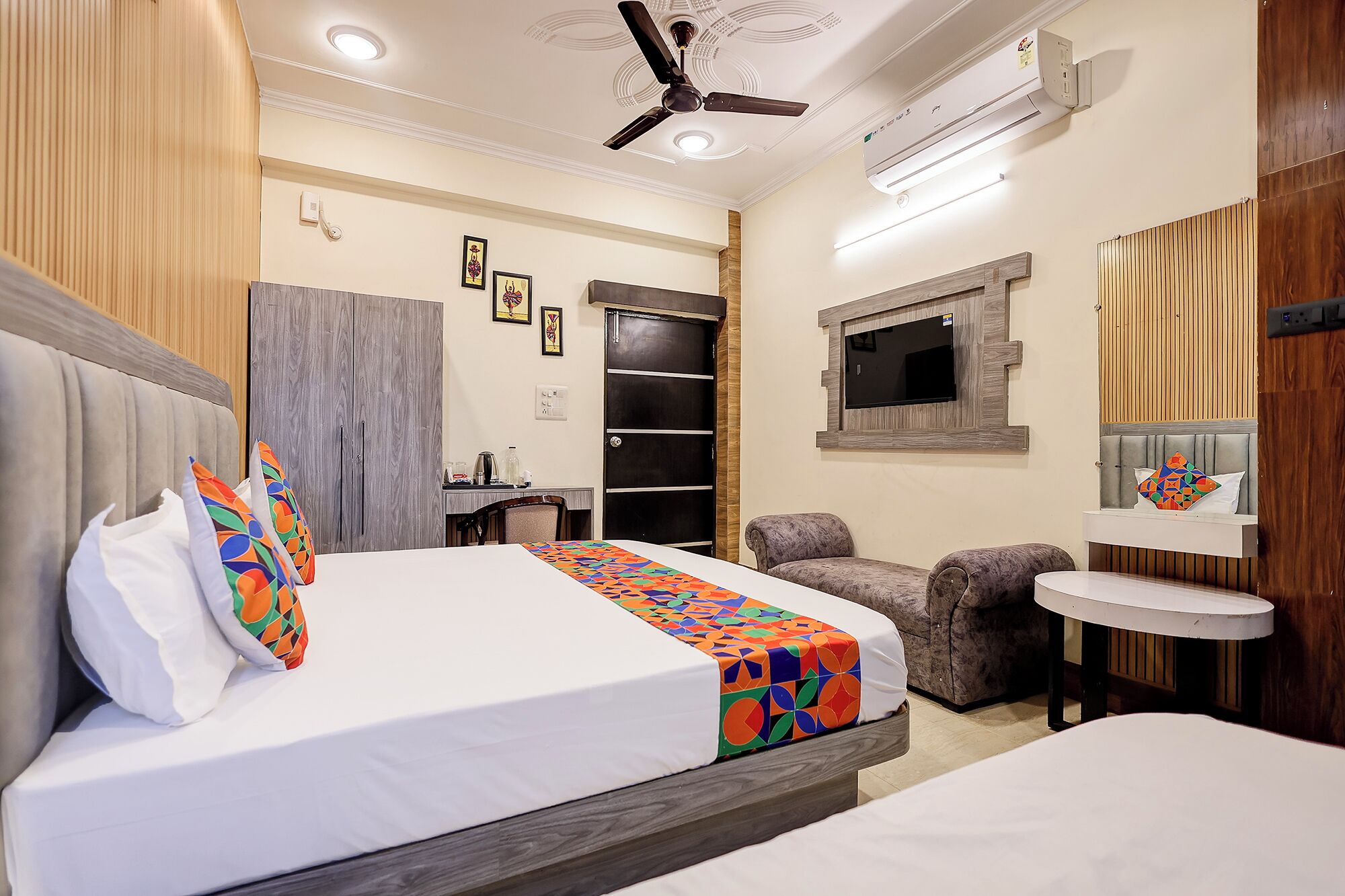 A hotel room with a bed, a desk, a chair, a small table, a TV, and a ceiling fan.