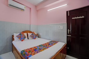 A bedroom with a bed, a wooden headboard, a dark door, and an air conditioning unit.