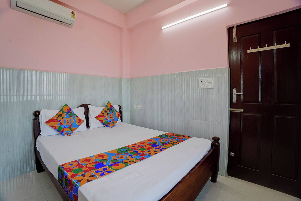 A bedroom with a bed, pillows, a bedside table, a door, and an air conditioning unit.