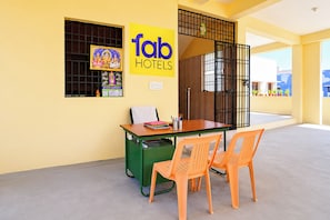 A hotel room with a desk, two chairs, a trash bin, and a window with artwork. - Fabhotel Madras Residency Nemili - Nr Rajiv Gandhi Memorial (Chennai)