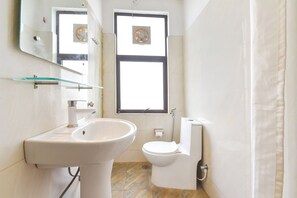 Et badeværelse med vask, toilet og et vindue med ventilator.