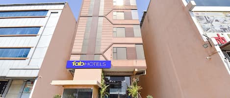 A modern hotel with a prominent 'fab hotels' sign, a staircase leading to the entrance, and potted plants at the base.