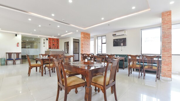 A spacious dining area with multiple wooden tables and chairs, a brick accent wall, and a flat-screen TV mounted on the wall. - Fabhotel Maru White Lotus (Jaipur)