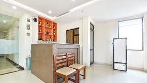 A clean, modern room with a wooden bench, a glass cabinet with bottles, and a large window. - Fabhotel Maru White Lotus (Jaipur)