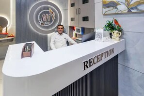 A reception desk with a logo, a plant, and a flag. - Fabhotel Mh Grand (Kalol)