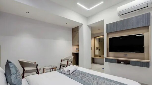 Une chambre d’hôtel moderne dotée d’un grand lit, d’un téléviseur fixé au mur, d’un petit coin salon et d’un appareil de climatisation.