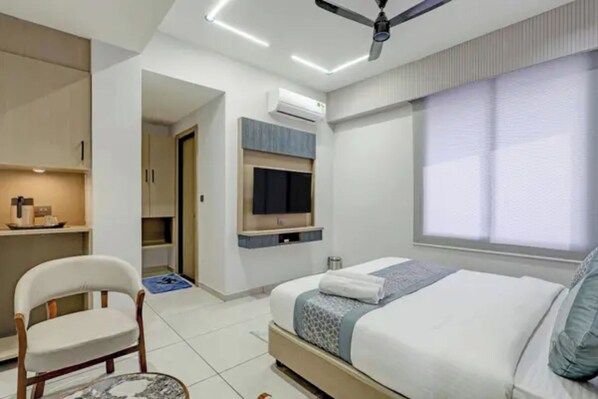 Una habitación de hotel moderna con una cama, una silla, un televisor y un equipo de aire acondicionado.