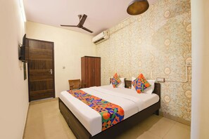 A bedroom with a bed, a ceiling fan, an air conditioning unit, a wooden wardrobe, and a patterned wall. - Fabhotel Mohan Villa (New Delhi)