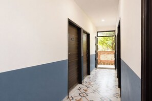 Un pasillo con suelo de baldosas, una puerta con número y vistas a zonas verdes al exterior.