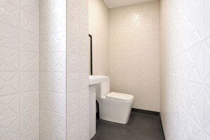 A small, narrow bathroom with white tiled walls and a white toilet. - Fabhotel Mohan Villa (New Delhi)