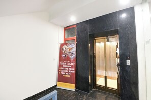 A hotel entrance with a red signboard advertising a deluxe room, a glass elevator, and a marble floor.