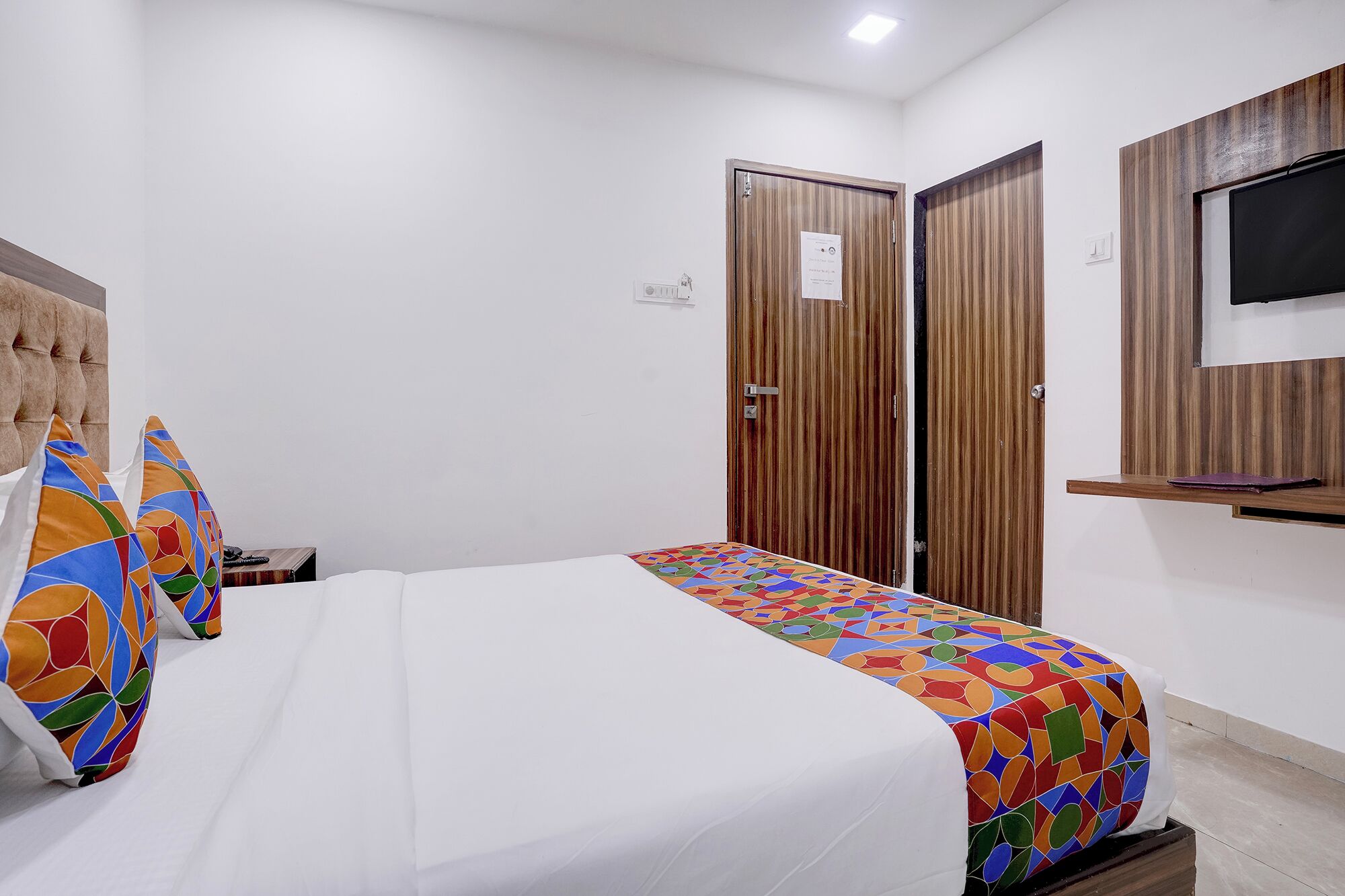 A bedroom with a bed, two doors, a television, and a small shelf.