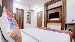 A hotel room with a bed, a TV, a desk with a bottle and glasses, and wooden paneling. - Hotel New Blue Sapphire Residency (Mumbai)