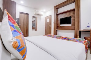 A hotel room with a bed, a TV, a desk with a bottle and glasses, and wooden paneling. - Hotel New Blue Sapphire Residency (Mumbai)