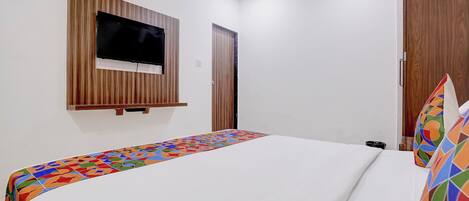 A hotel room with a bed, a television mounted on the wall, and a door.