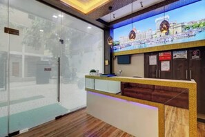 Un mostrador de recepción con un separador de vidrio, una pantalla digital y suelo de madera.