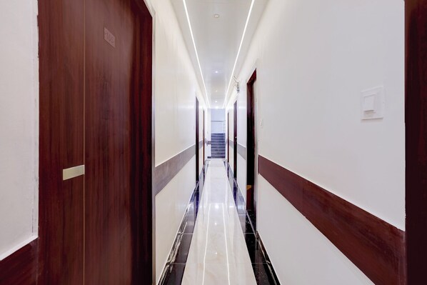 Un passadís d'hotel amb una porta de fusta, un paviment de marbre i una escala al final.