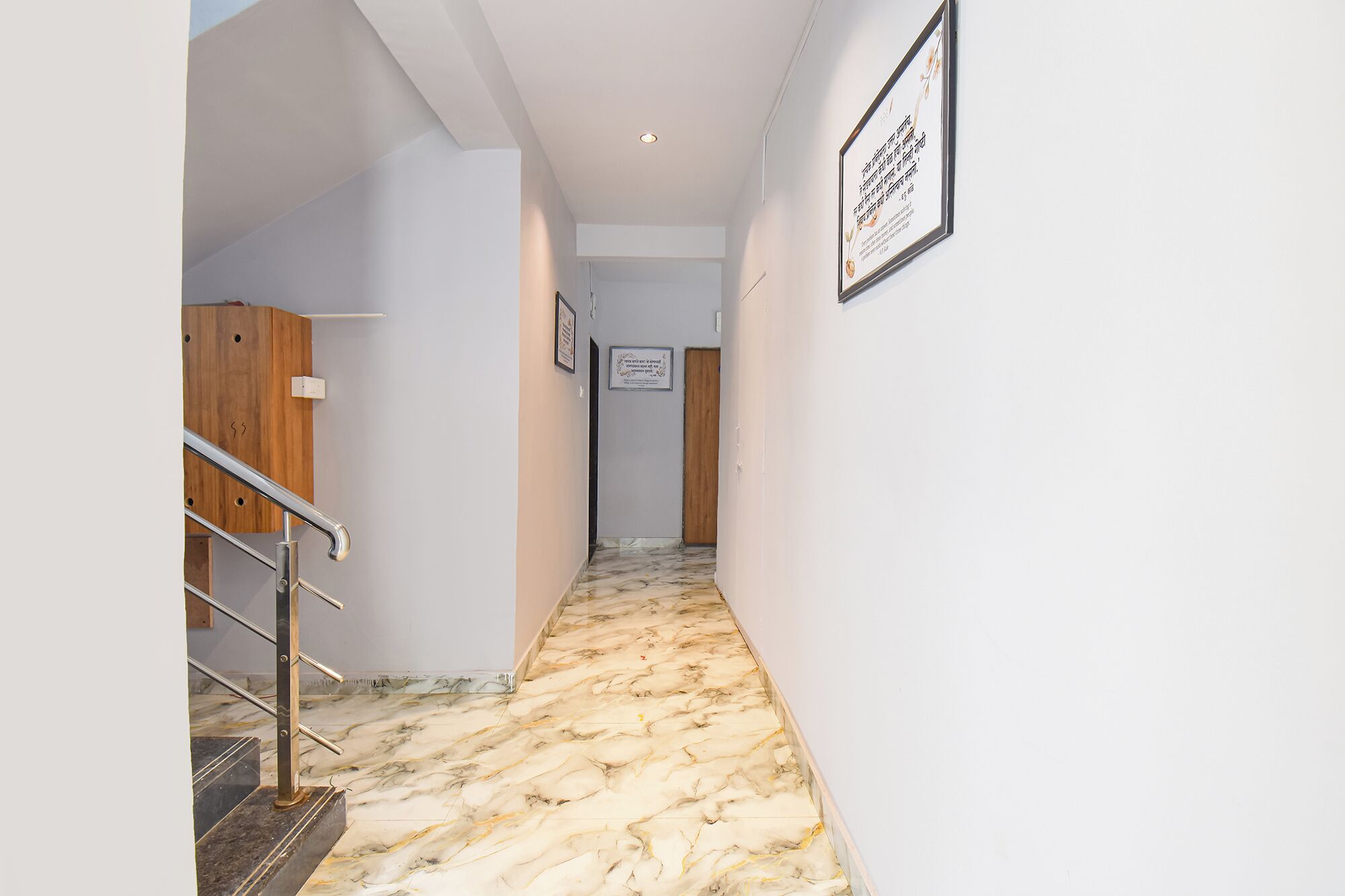 A hallway with a marble floor, a wooden door, and a framed sign on the wall.