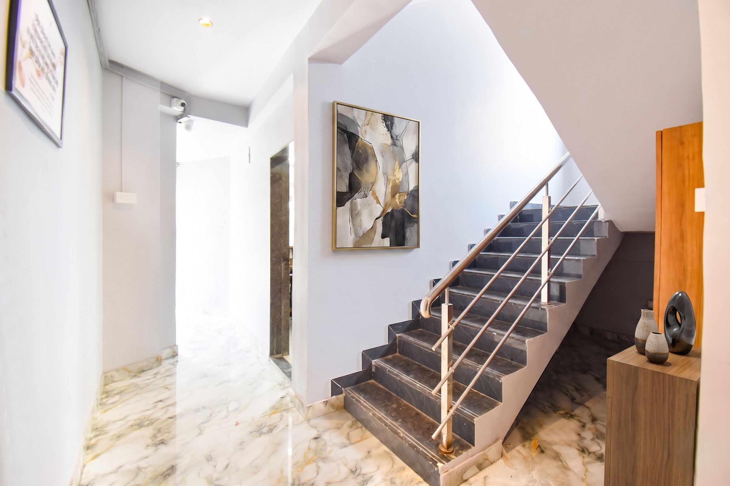 A modern staircase with a glass railing, marble flooring, and a contemporary abstract painting on the wall.