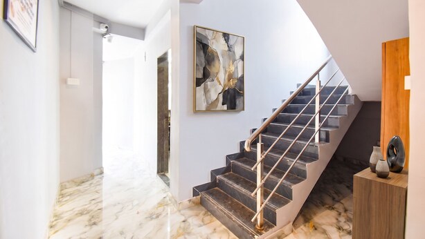 Una escalera moderna con barandilla de vidrio, suelo de mármol y un cuadro abstracto contemporáneo en la pared.