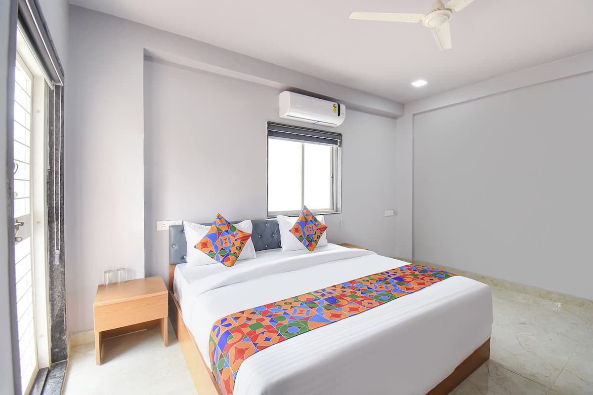 Un dormitorio con una cama, una ventana, aire acondicionado, ventilador de techo y una mesita de noche de madera.