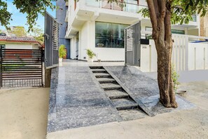 Un moderno edificio residencial con entrada pavimentada, un árbol y un camino de acceso con puerta.