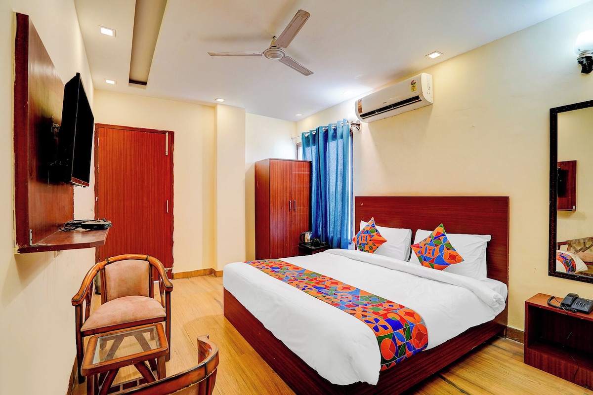 Quarto de hotel com cama, cadeira, guarda-roupa, escrivaninha, espelho e ar condicionado.