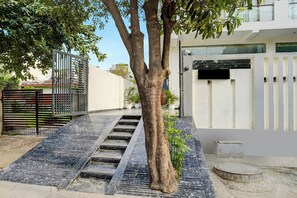 Una entrada cerrada con un árbol, escalones que conducen a una puerta y un edificio blanco al fondo.