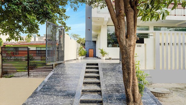 Un edificio moderno con una escalera que lleva a una puerta, rodeado de árboles y una entrada con reja.
