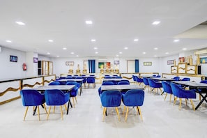 Un salón de conferencias con mesas y sillas, paredes blancas e iluminación en el techo.