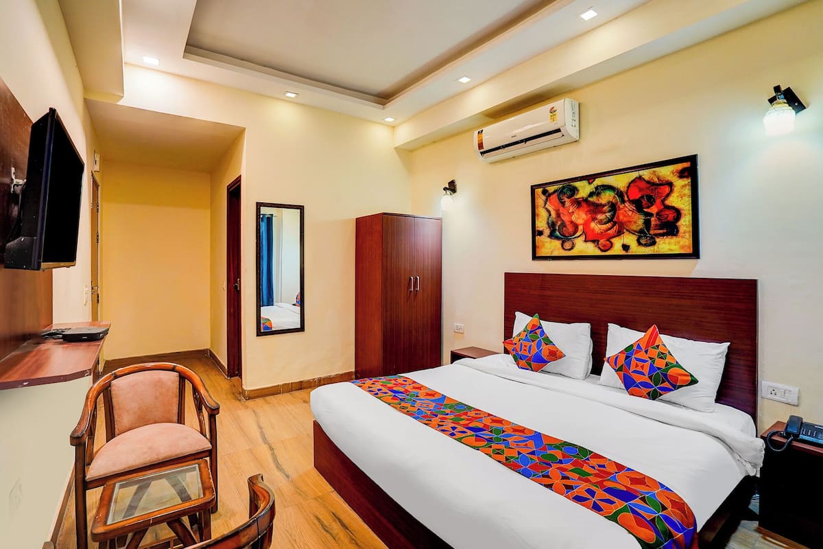 A hotel room with a bed, a chair, a wardrobe, an air conditioning unit, a painting, and a telephone.