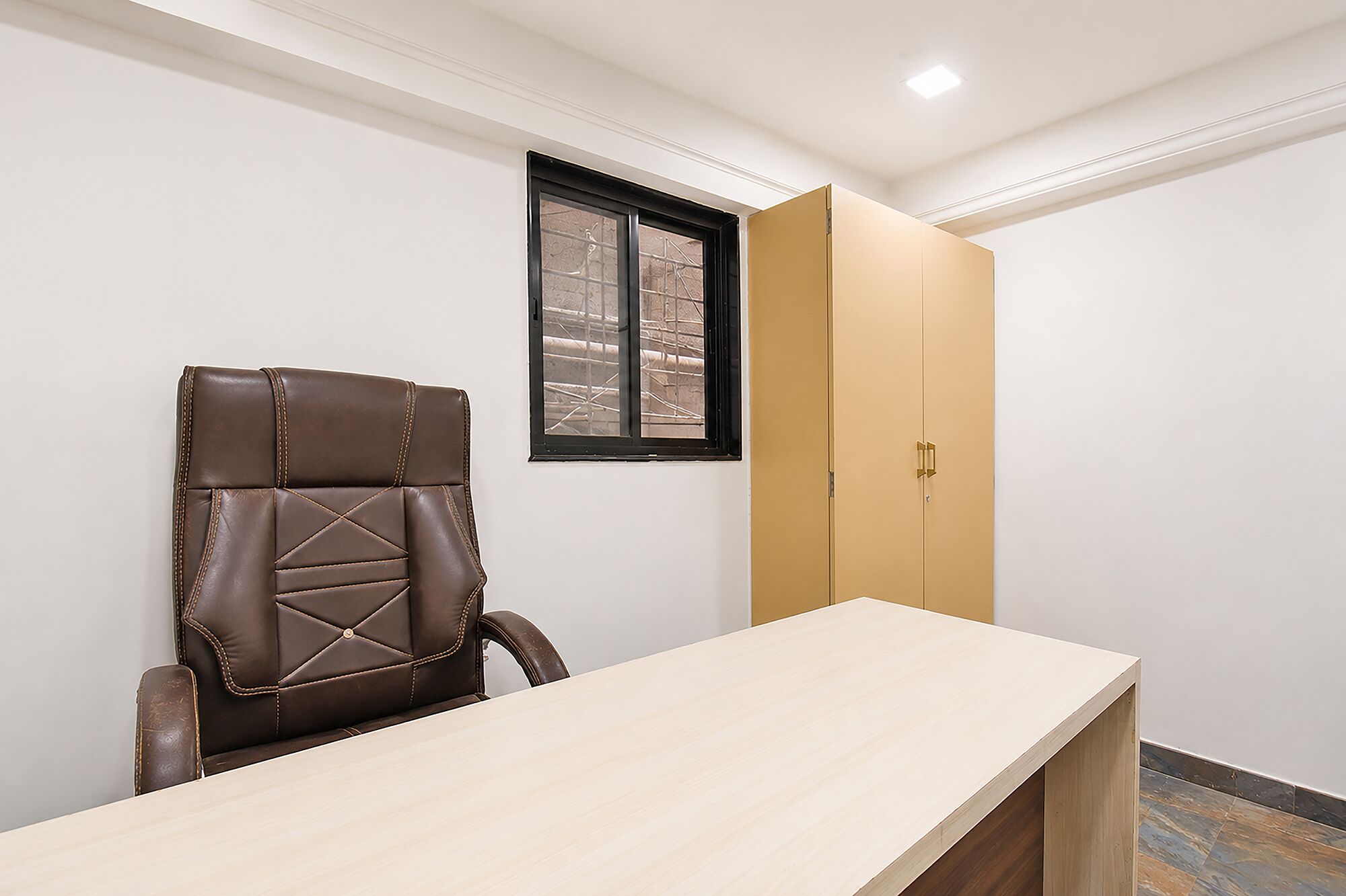 A room with a wooden desk, a brown leather chair, a window, and a wardrobe.