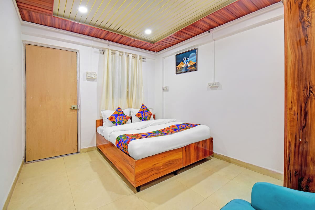 Un dormitorio con una cama de madera, paredes blancas, techo con vigas de madera, una puerta y un cuadro.