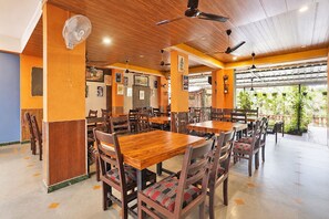 Ein Restaurant mit Holztischen und -stĂŒhlen, Deckenventilatoren und Blick auf GrĂŒnflĂ€chen.