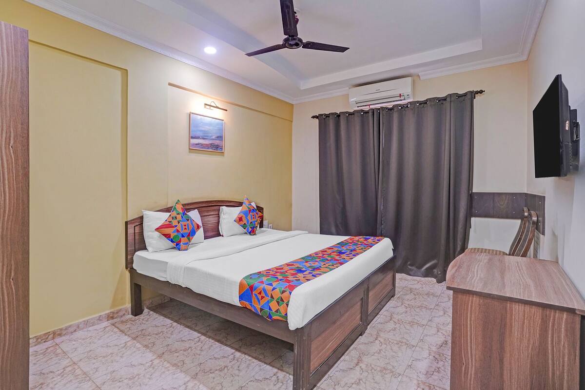 A hotel room with a bed, a desk, a ceiling fan, an air conditioning unit, and a television.