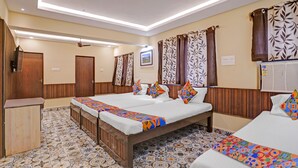 A hotel room with two beds, a wooden wardrobe, a small desk, and patterned floor tiles.