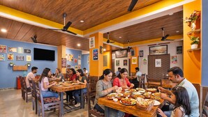 A restaurant with wooden tables and chairs, a TV mounted on the wall, and various posters and signs.