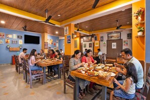 Um restaurante com mesas e cadeiras de madeira, uma televisão na parede e diversos cartazes e placas.
