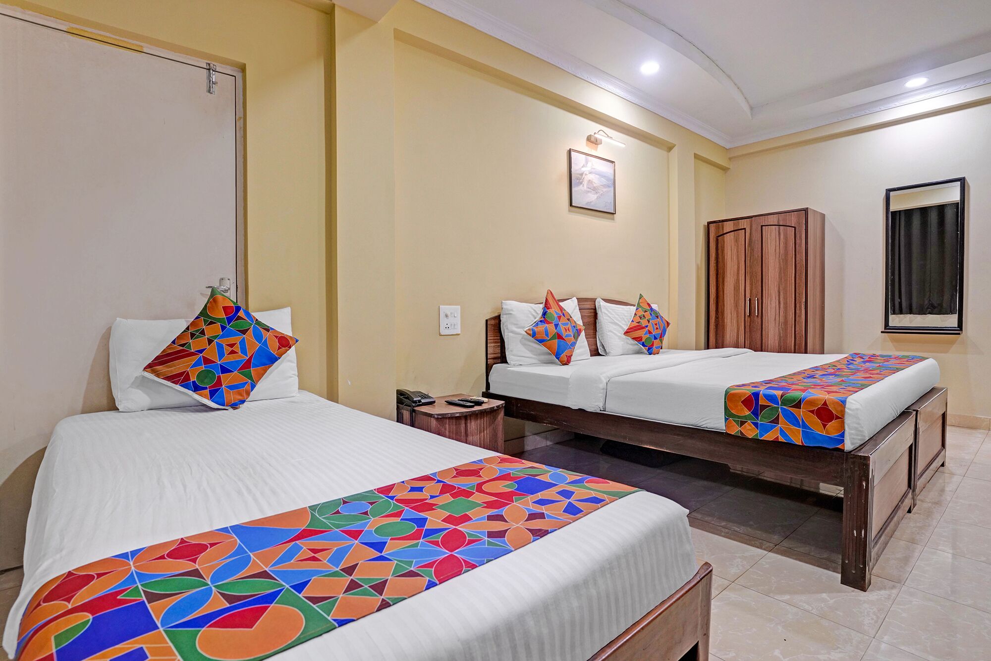 Quarto de hotel com duas camas, um guarda-roupa de madeira, uma mesinha de cabeceira e um quadro na parede.