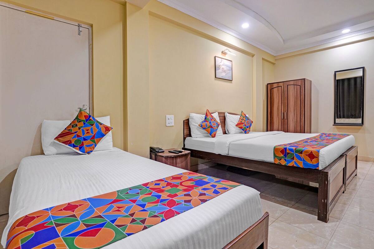 A hotel room with two beds, a wooden wardrobe, a bedside table, and a framed picture on the wall.