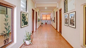 A hallway with framed pictures on the walls, potted plants, and a tiled floor.