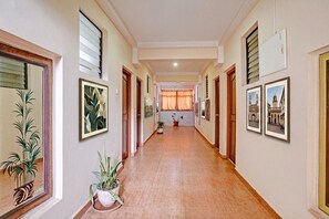 Um corredor com quadros nas paredes, plantas em vasos e piso de azulejos.