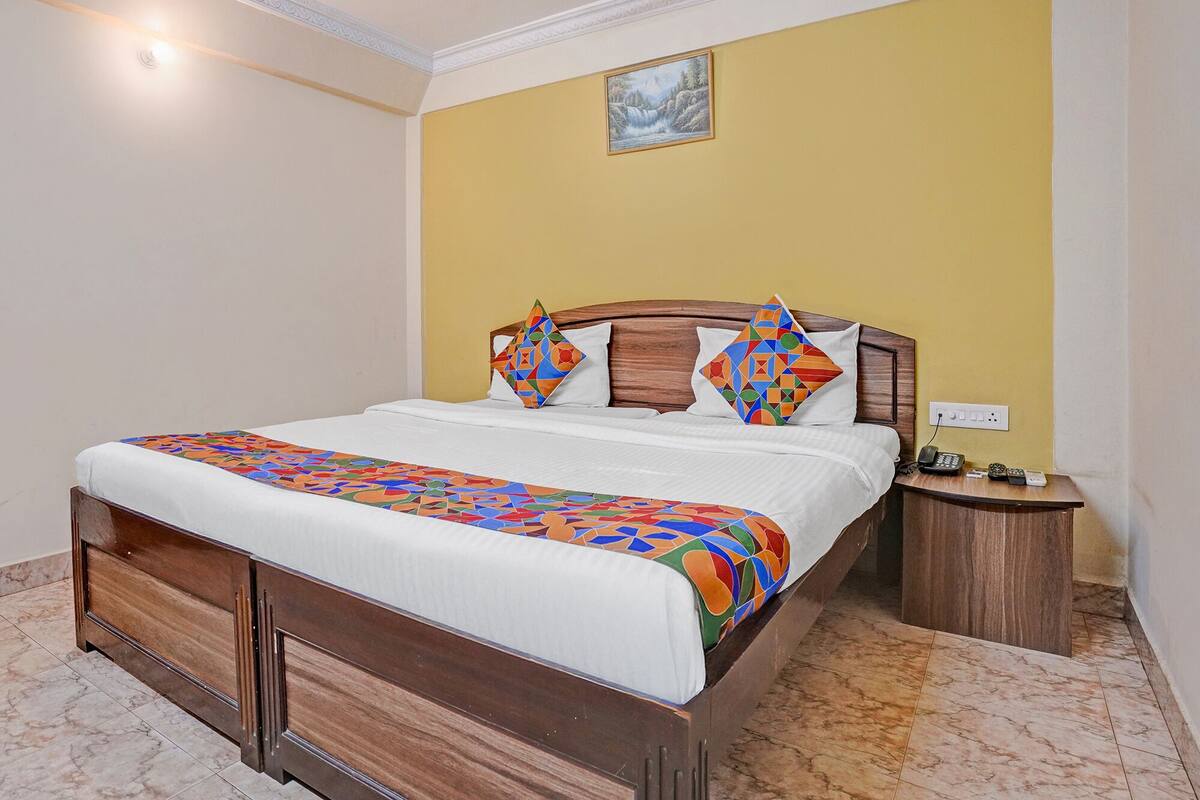 A bed with a wooden frame, a white bedspread, and colorful geometric pillows.