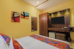A hotel room with a bed, a desk, a television, and two paintings on the wall.