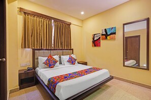 Habitación de hotel con cama, mesita de noche con teléfono, cuadro colgado en la pared y puerta con espejo.