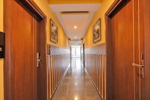 A hotel hallway with wooden doors, a polished floor, and framed artwork on the walls. - Fabhotel Pride (Bangalore)