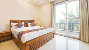 A modern hotel room with a large bed, a nightstand, a window with a view of greenery, and a balcony. - FabHotel Prime Hush & Suites - Manesar and Sector 86 (Gurugram)
